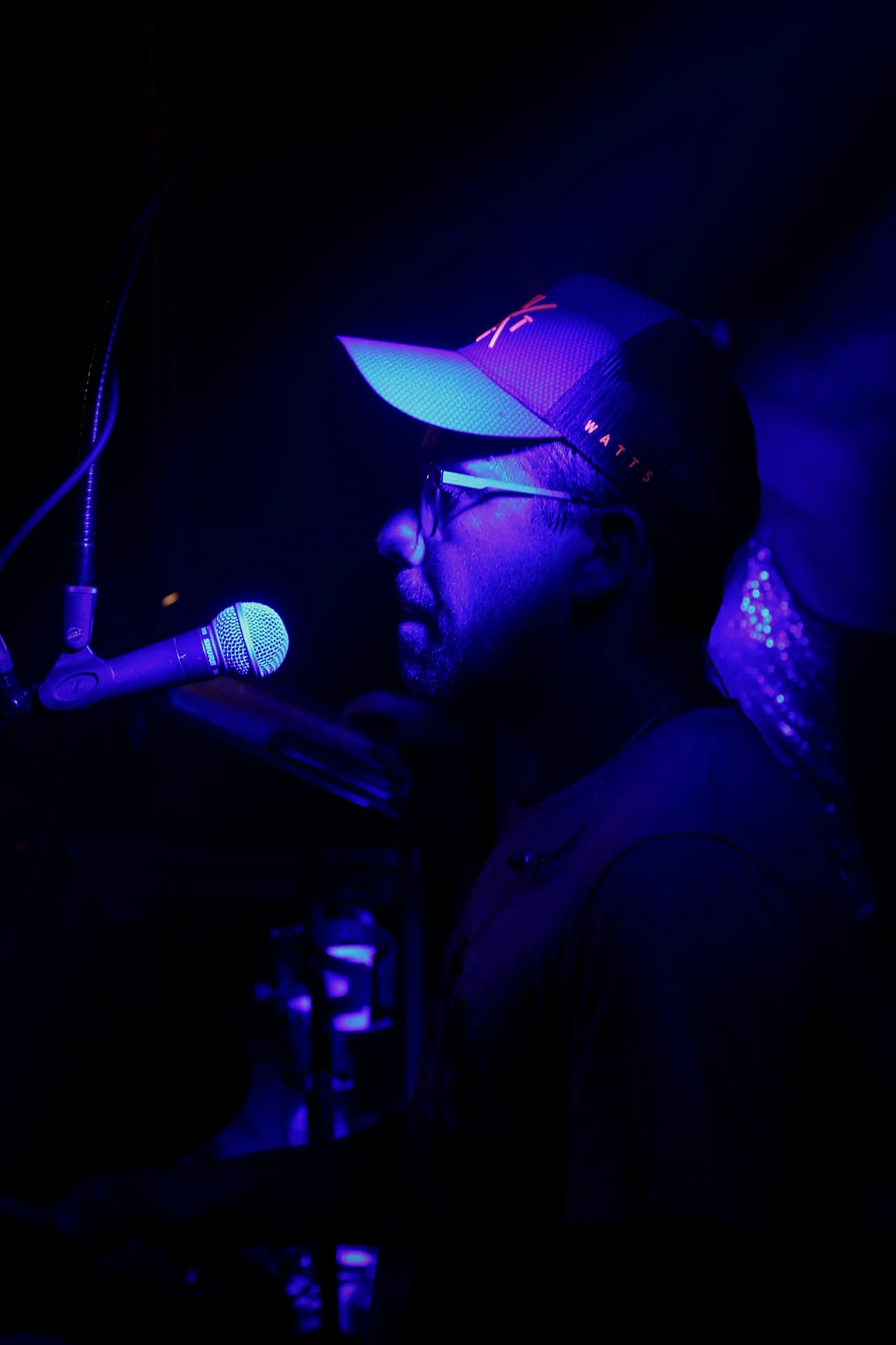 Chanteur de Watts Up au micro, casquette du groupe, sous les lumières bleues